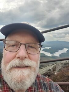 Glenn D’Alessio lives in West Brookfield, MA with his wife. His first class in poetry was taken
at North Country Community College in Saranac Lake, NY. It focused on the beats. Much more
valuable to Glenn was a class about short stories by Patricia Wiley. He also adopted his first
dog, Seico, then. She was a white dog with a ring around one eye and her tail. During 1971 the
two of them spent summer in a homemade lean-to at Caulkin’s Creek in the Adirondacks. He
has never been without a dog since.
One of Glenn’s most productive periods of writing was last decade. Elroy deserves credit. “My
Hero// My Hero cheers me whenever I come Home/ from whatever day’s stressful complaints/
and paints me an alternative universe/ of tranquil seas and gentle breeze/ so our hearts will ease.”
For a small rat terrier, Elroy was fearless of any dog or person, regardless to size, and was most
gregarious. There was only one exception. “Cameras// Elroy was from/ one of those cultures/
whose soul would be/ snared by a camera's// shutter grabbing/ feet or eyes,/ so his would go/ to
Elysian fields,// or toward the nearest/ inanimate/ couch or table,/ both totems to protect// his
curly tail/ late behind him,/ not wanting to become/ locked into a box.” This phobia was like
Glenn’s childhood worry that something would sneak up behind him. That’s why he would
circle to unwind himself on landings, and at the tops to stairs. In doing this he could see what
was behind – his winding like Elroy’s tail.
They were both cantankerous, but on a midnight walk in starlight or first thing in the morning
they would strike a balance. Elroy would be on a leash so he wouldn’t get lost and die. Thus,
Glenn considered a little restraint to be for Elroy a “Freedom of the Leash// He pulls and I push./
I’m small, trotting to his walking,/ and I’m in no rush/ when he has to go to work./ We find a
happy medium.” The two of them were like a match made in heaven.